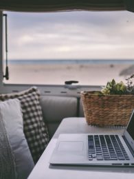 Remote onilne work and smart working travel concept with laptop computer inside a van camper interior with beach view. Freedom from office modern lifestyle for alternative life and people
